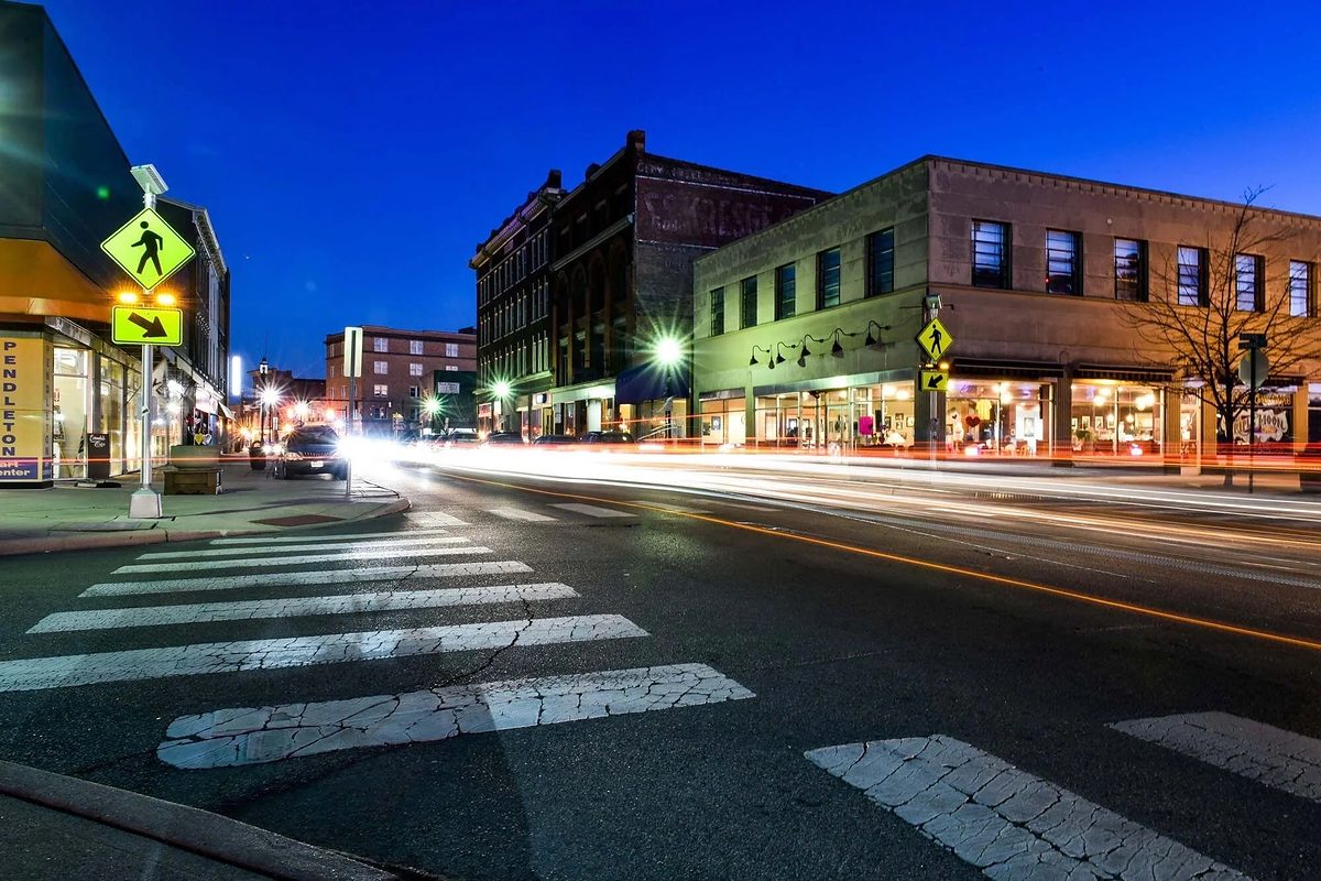 Main Street in Middletown at blue hour, lit shopfronts along a row of nineteenth-century brick buildings with car light trails across the foreground